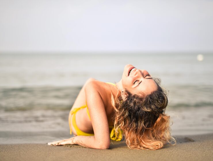 SheJournal | A woman embracing body awareness and feminine confidence by the sea, representing self-love and emotional healing