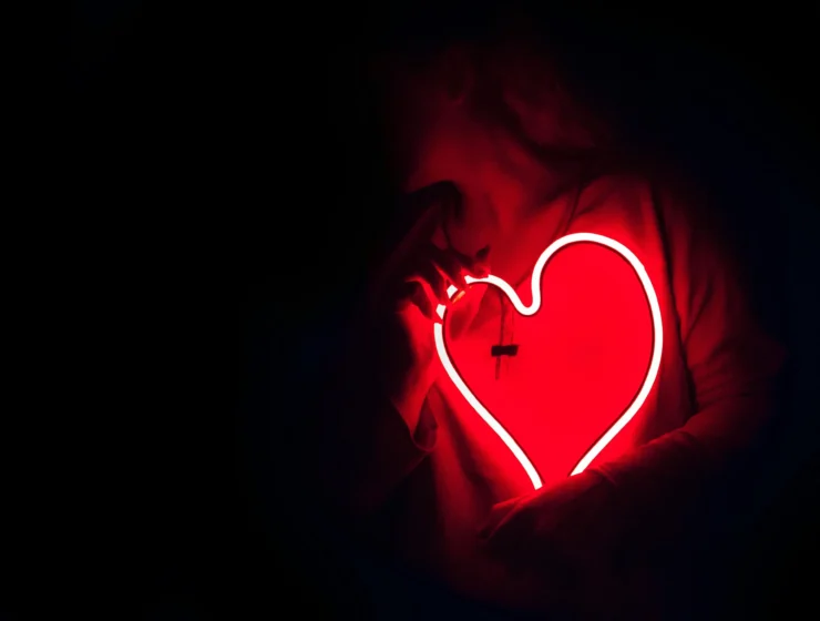 A woman holding a glowing red heart light in the dark, symbolising emotional clarity and self-awareness in modern relationships.