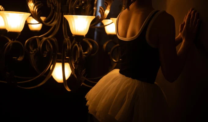A woman standing in soft chandelier light, expressing quiet self-reflection and feminine confidence