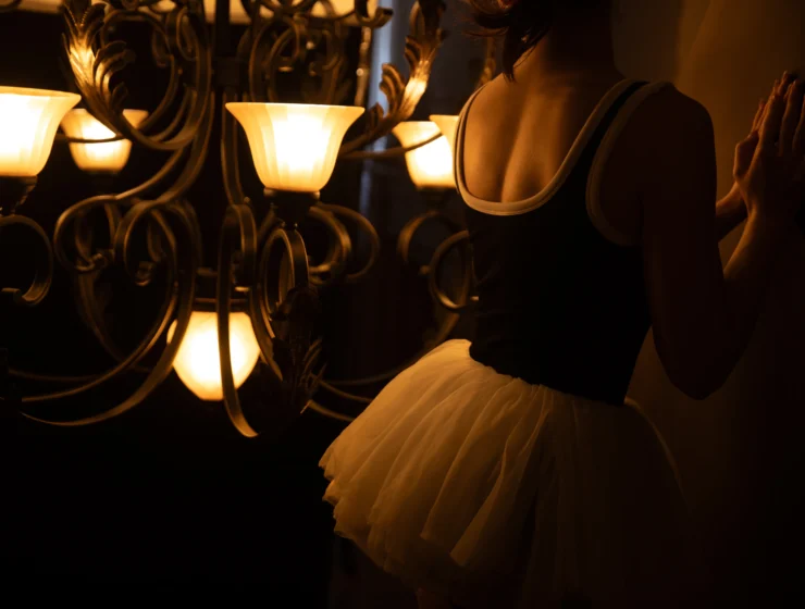 A woman standing in soft chandelier light, expressing quiet self-reflection and feminine confidence