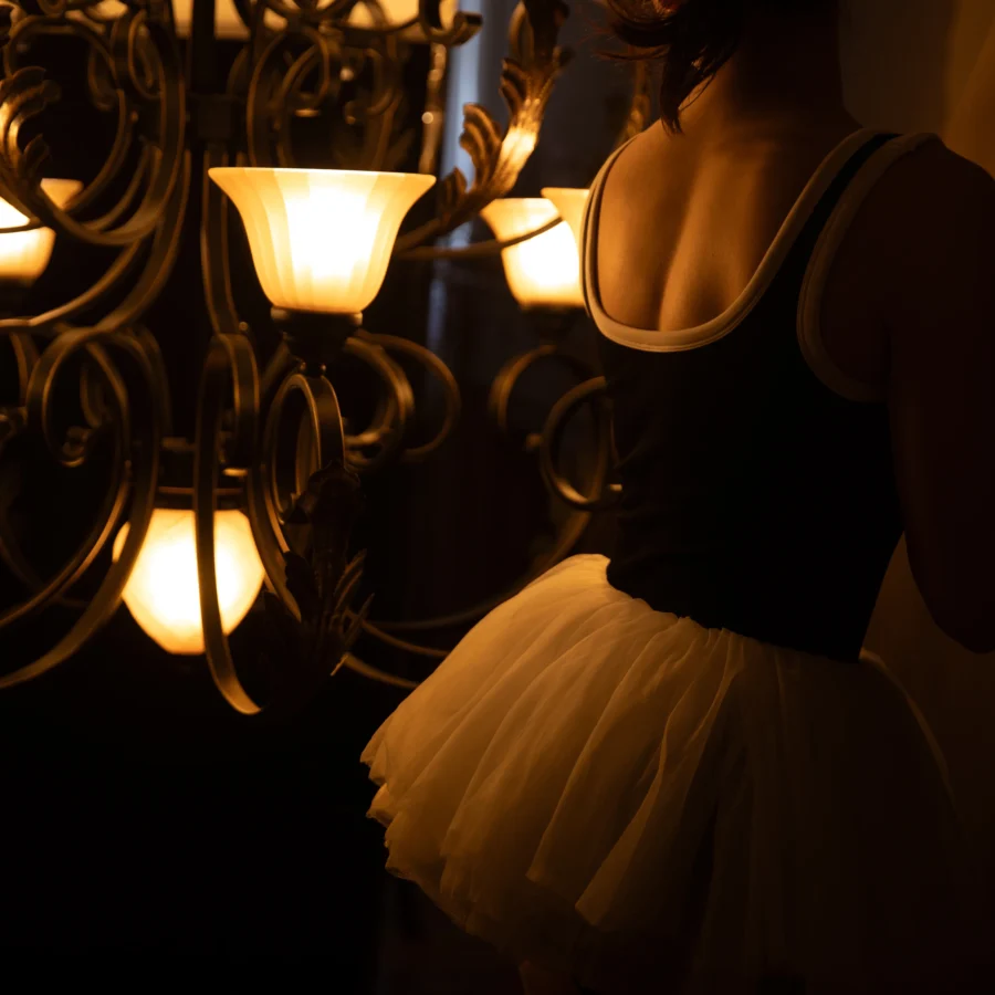 A woman standing in soft chandelier light, expressing quiet self-reflection and feminine confidence