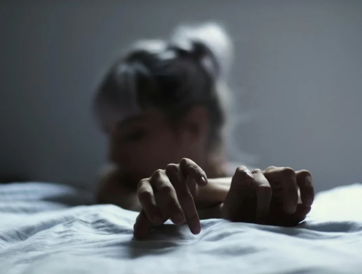 Woman’s hands resting on a rumpled bed in soft blue night light, symbolising replaying every conversation at 3 a.m.