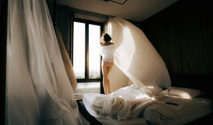 Woman standing by a window in soft morning light, symbolizing quiet reflection and emotional clarity before making a decision.