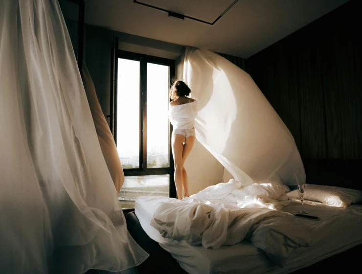 Woman standing by a window in soft morning light, symbolizing quiet reflection and emotional clarity before making a decision.