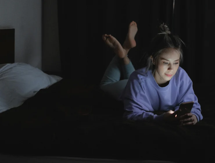 Young woman lying in bed at night texting on her phone